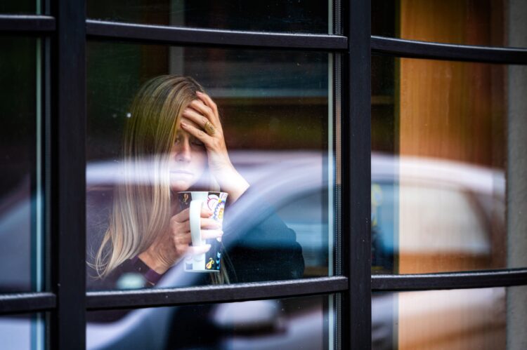Smutna kobieta stoi przy oknie trzymając kubek herbaty w dłoni