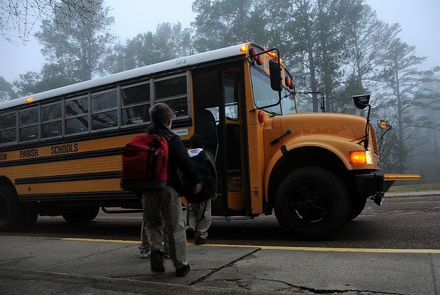 Dzieci wchodzą do autobusu szkolnego i mają na sobie plecaki i tornistry