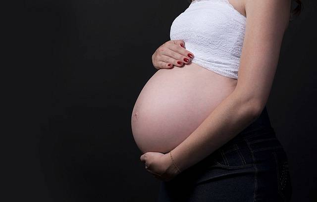 Kobieta w ciąży trzyma swój duży brzuch rękami i zastanawia się nad akcesoriami które mogą się jej przydać
